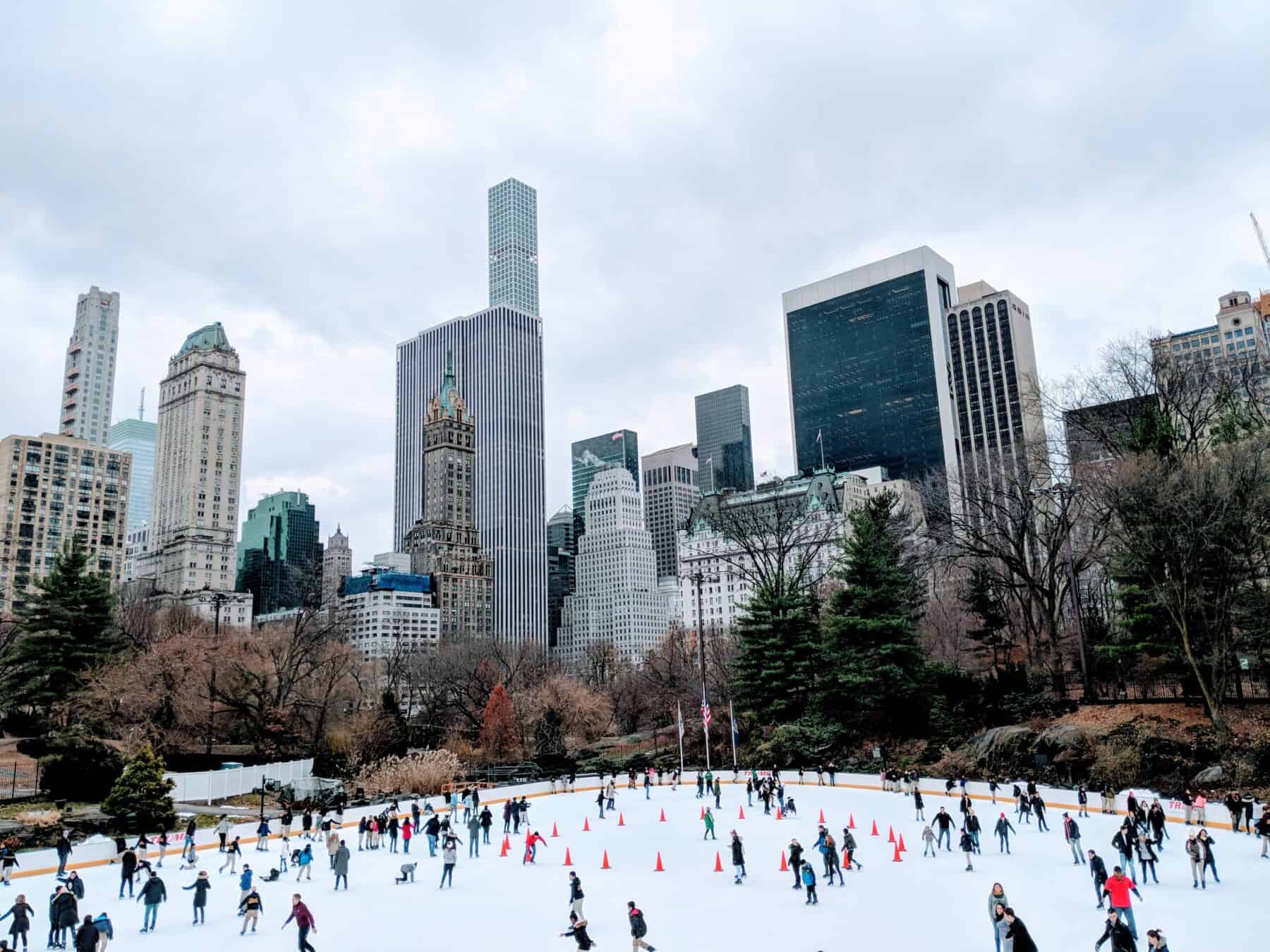 people ice skating outdoors surrounded by tall buildings