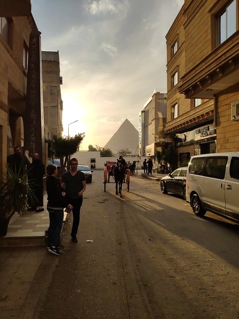 The shadow of a pyramid in the background of a street in Cairo as the sun sets. Image source: Pixabay user Photoholiday.