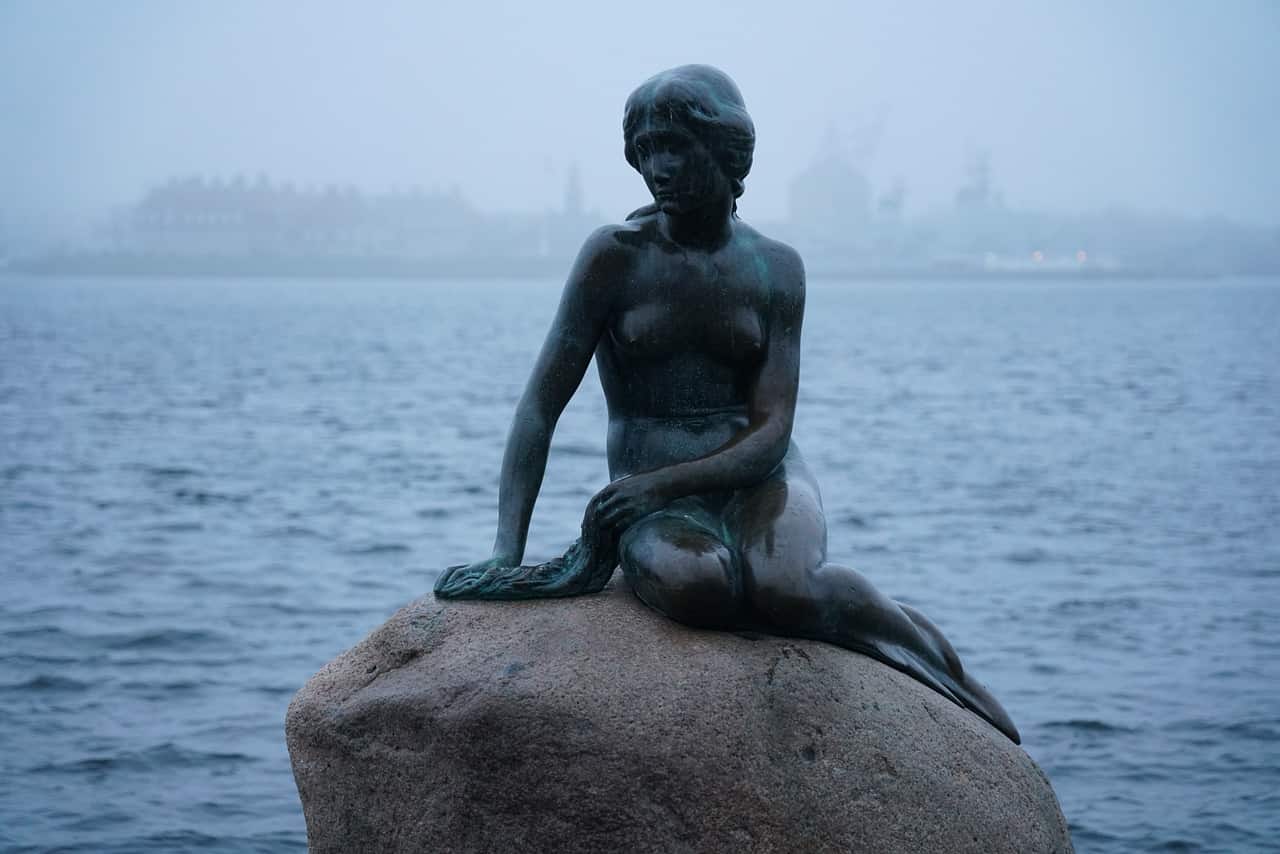 The Little Mermaid Statue sitting on a rock in the water.