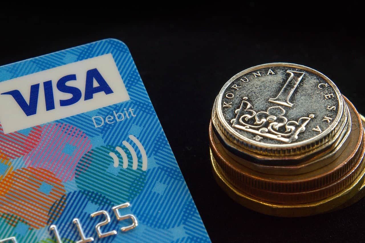 A debit card next to a pile of Czech koruna coins. Image source: Pixabay user Miloslav Hamrik.