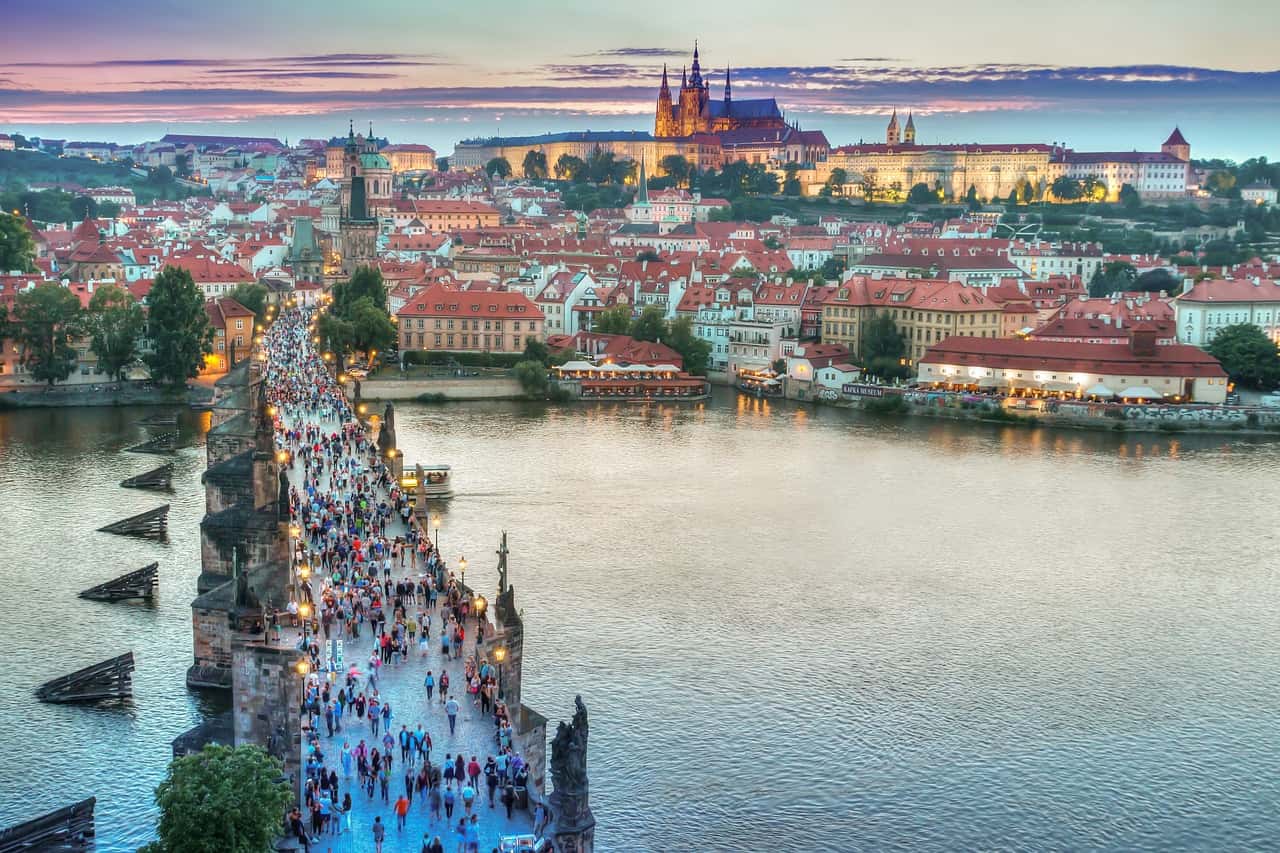 Sunset over Prague with people lining the Charles Bridge.