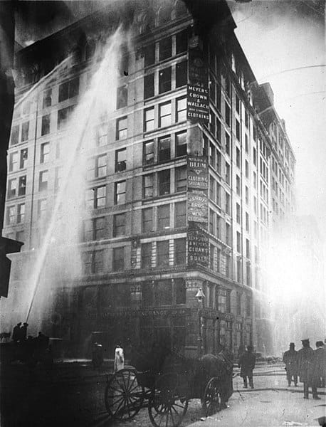 An actual photo of the Triangle Shirtwaist Factory fire in 1911. Image Source: Wikimedia under public domain (image is more than 95 yrs old).